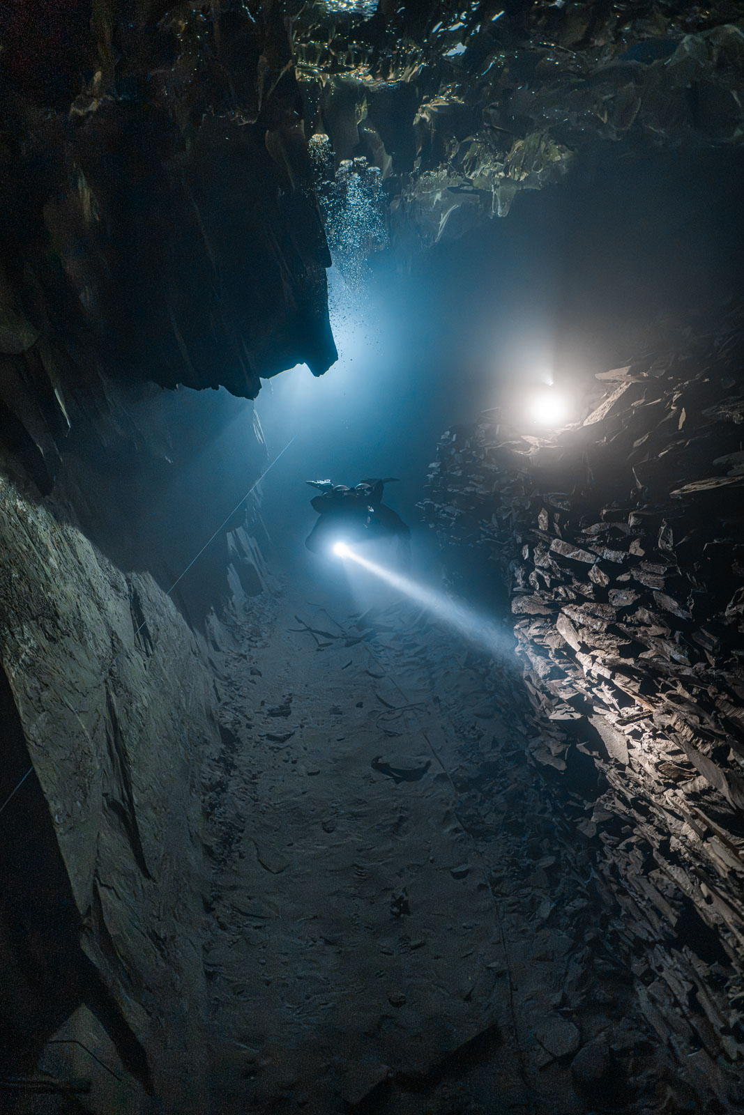 Zwei Taucher mit Lampen in einem felsigen Bergwerksgang