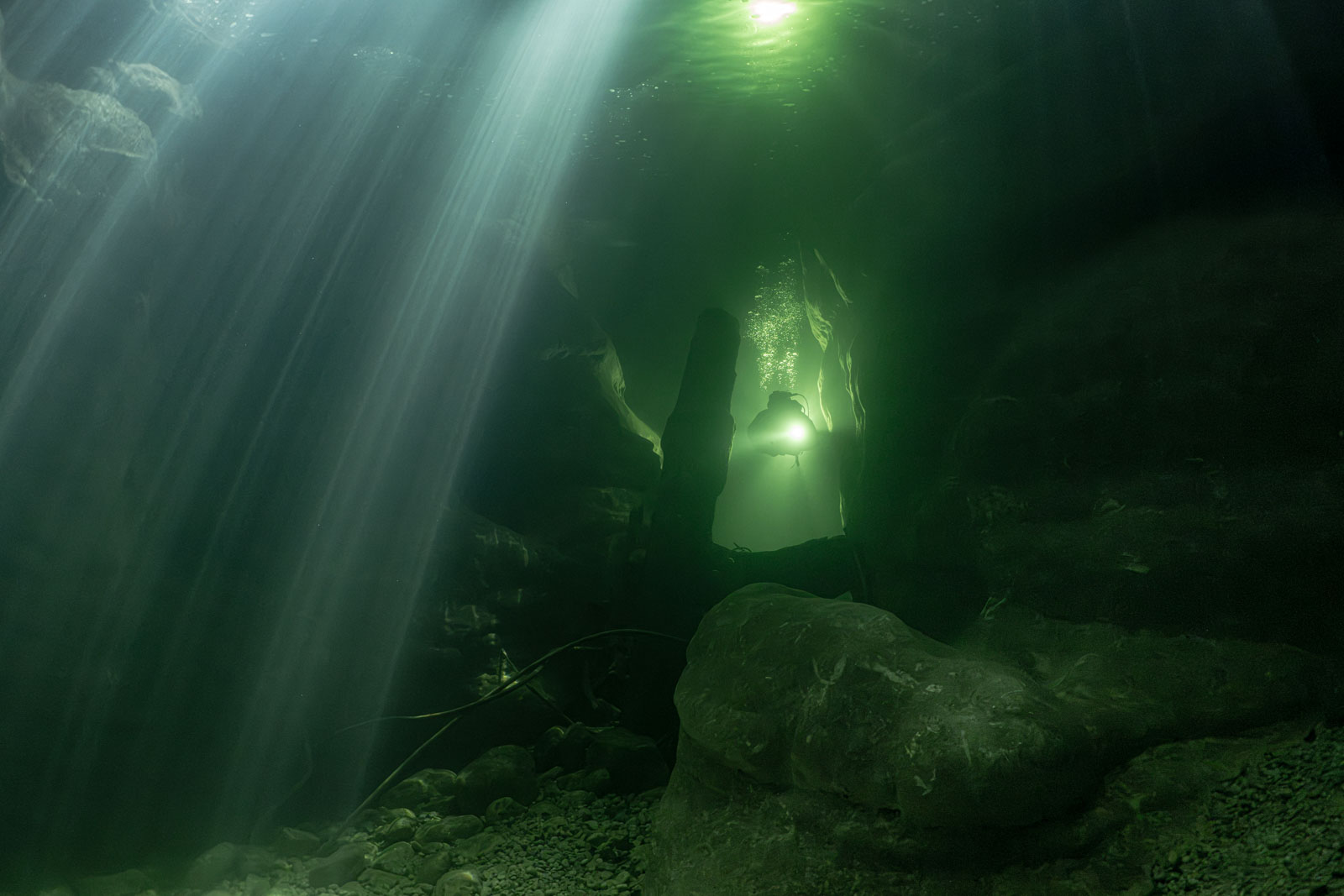 Diver among rocks in green water with sunbeams