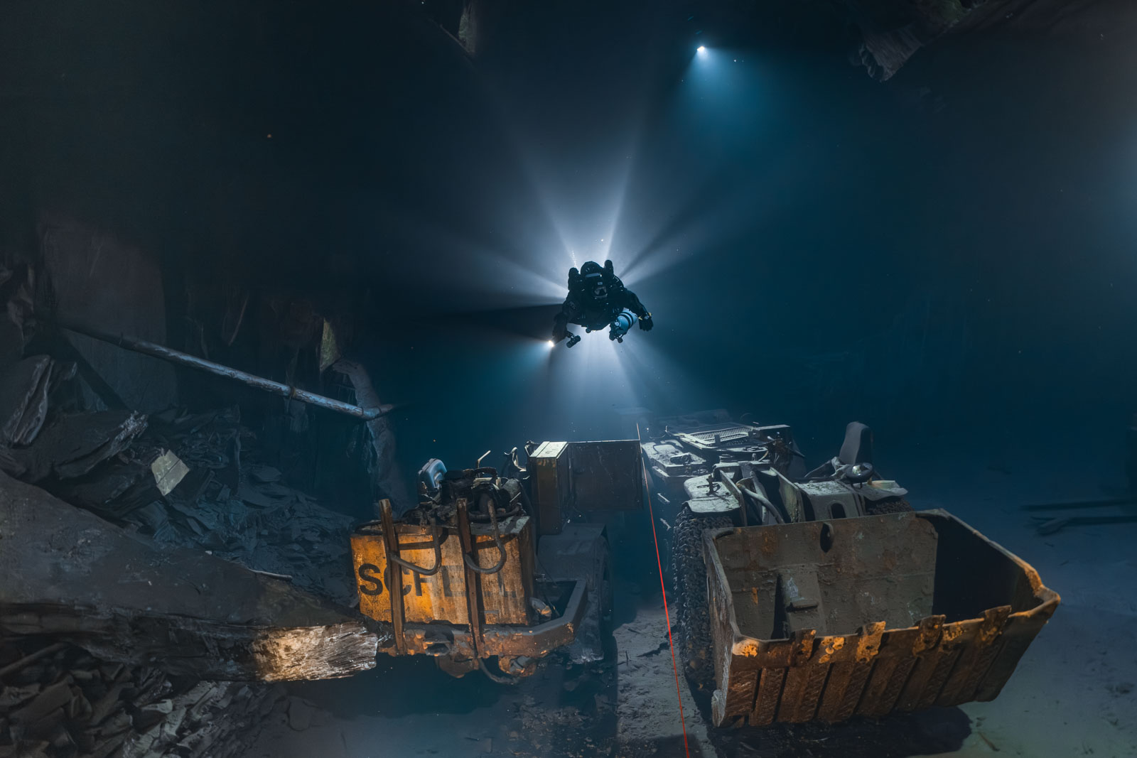 Taucher mit fächerförmigen Lichtstrahlen über einer alten Bergwerksmaschine