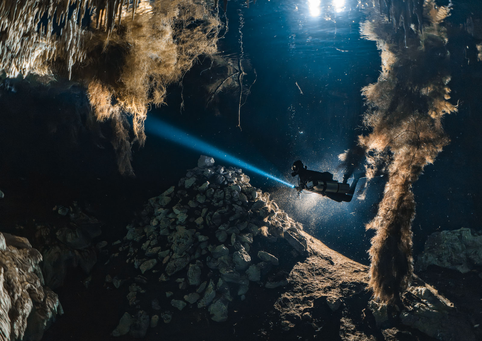 Taucher mit Lichtstrahl unter einer spiegelnden Wasseroberfläche in einer Höhle