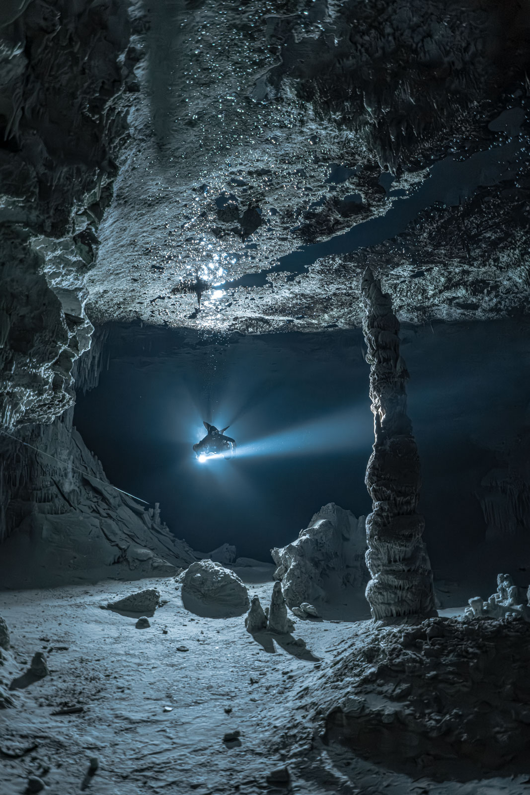 Lichtstrahl eines Tauchers hinter hellen Tropfsteinen